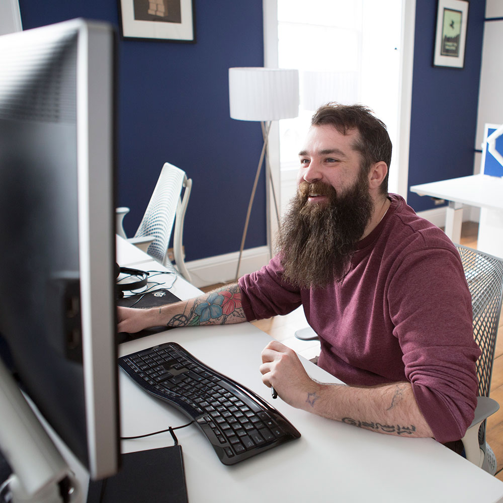 A smiling man with a beard working at an ergonomic desk.
